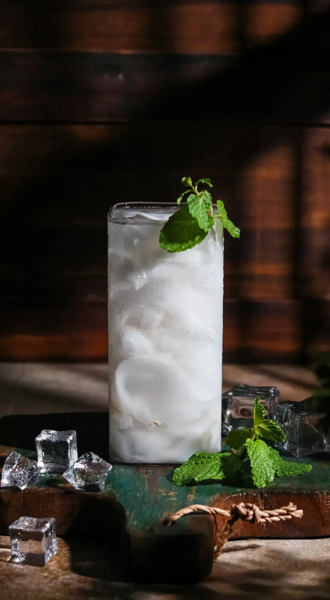 Tall glass of chilled mojito cocktail garnished with fresh mint sprigs and filled with ice cubes, professional food service presentation.